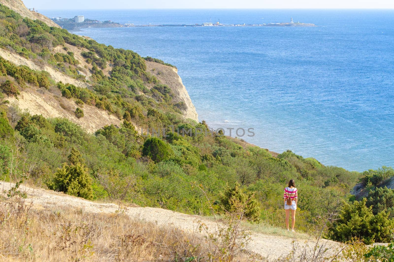 A girl stands on a hill and looks into the distance at the sea