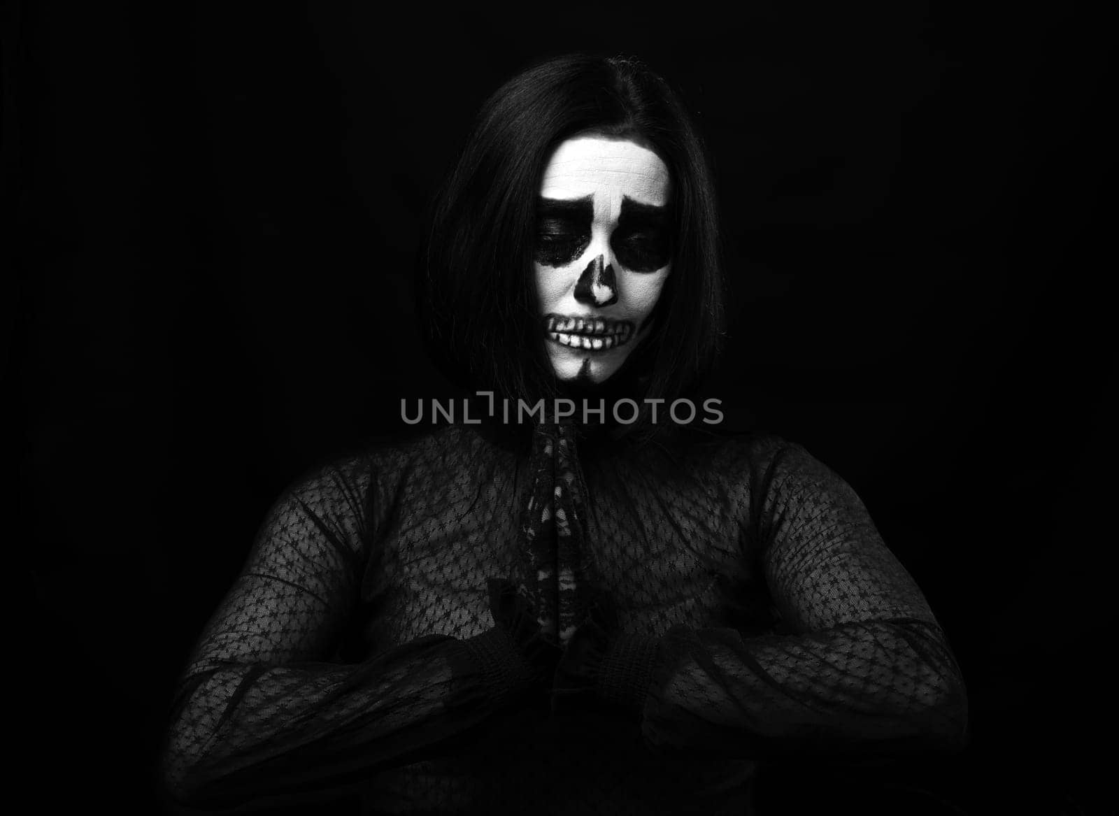 woman with skeleton make-up stands in prayer pose, black background