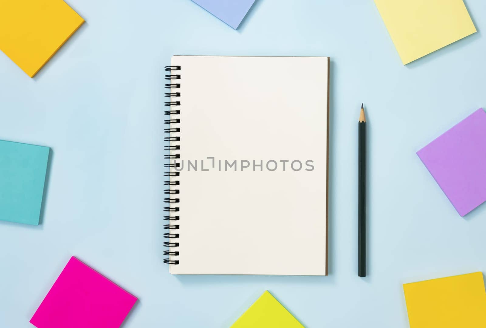 Spiral Notebook or Spring Notebook in Unlined Type and Multi Color Sticky Note and Pencil on Blue Pastel Minimalist Background. Spiral Notebook Mockup on Center Frame
