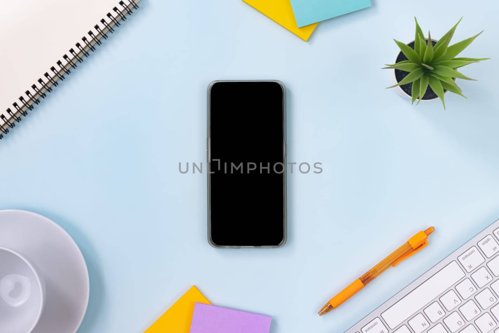 Vertical Mobile Phone or Smartphone and Office Supplies as Keyboard,Pen,Sticky Note,Office Plants,Spiral Notebook,Coffee Cup on Modern Clean Creative Office Desk or Table on Top View or Flat Lay