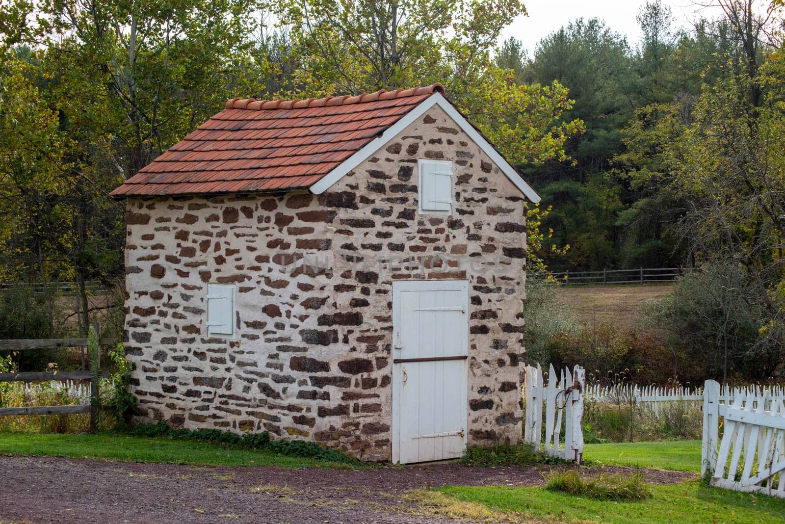 Idyllic country scene with a colonial stone spring house, by a white garden gate and idyllic Autumn woodland landscape background.
