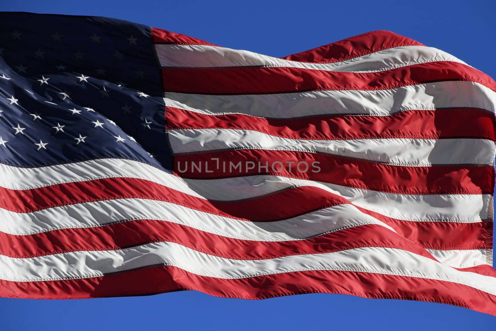 The American flag is waving in the wind. Stars and stripes can be seen on the USA flag.