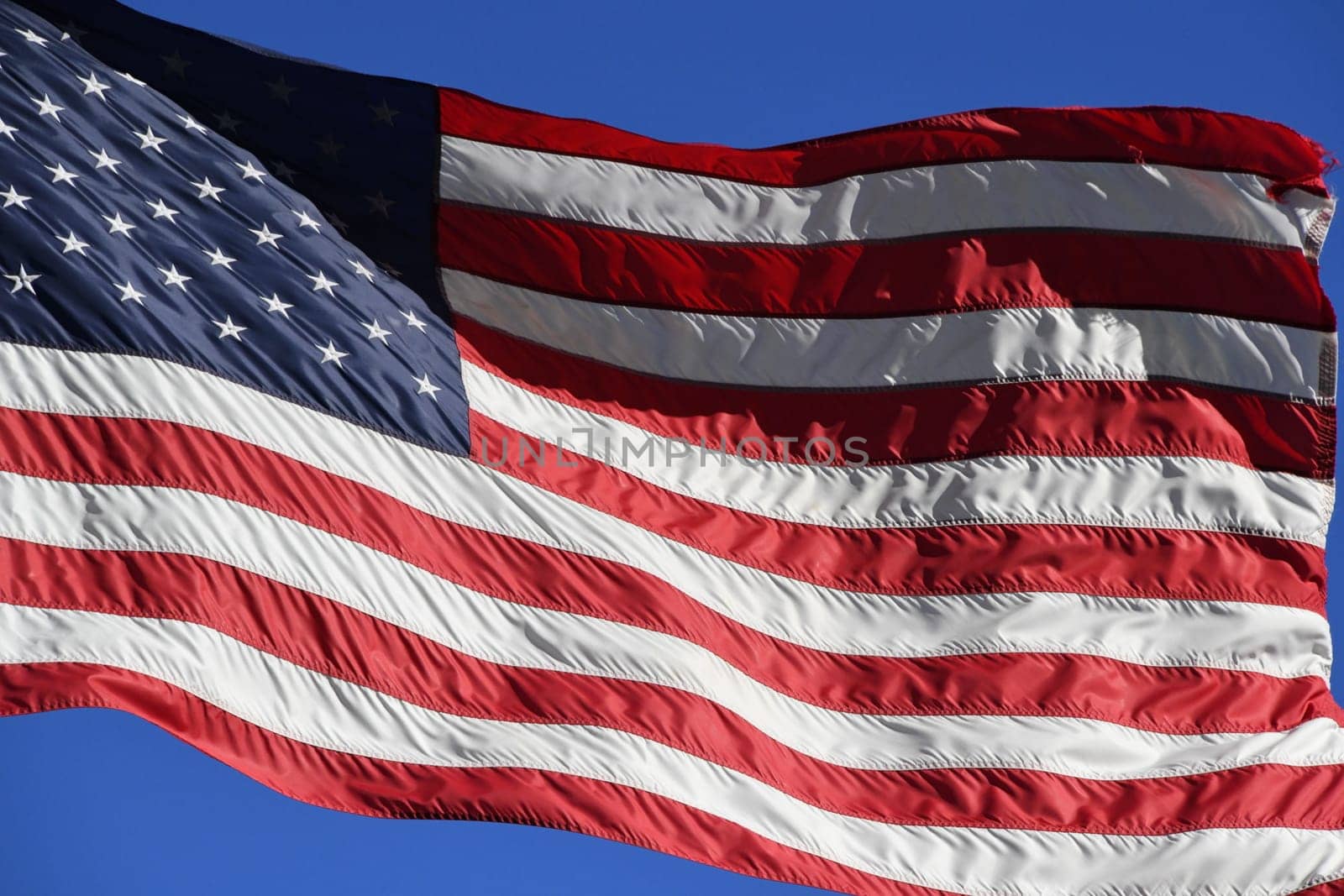The American flag is waving in the wind. Stars and stripes can be seen on the USA flag.