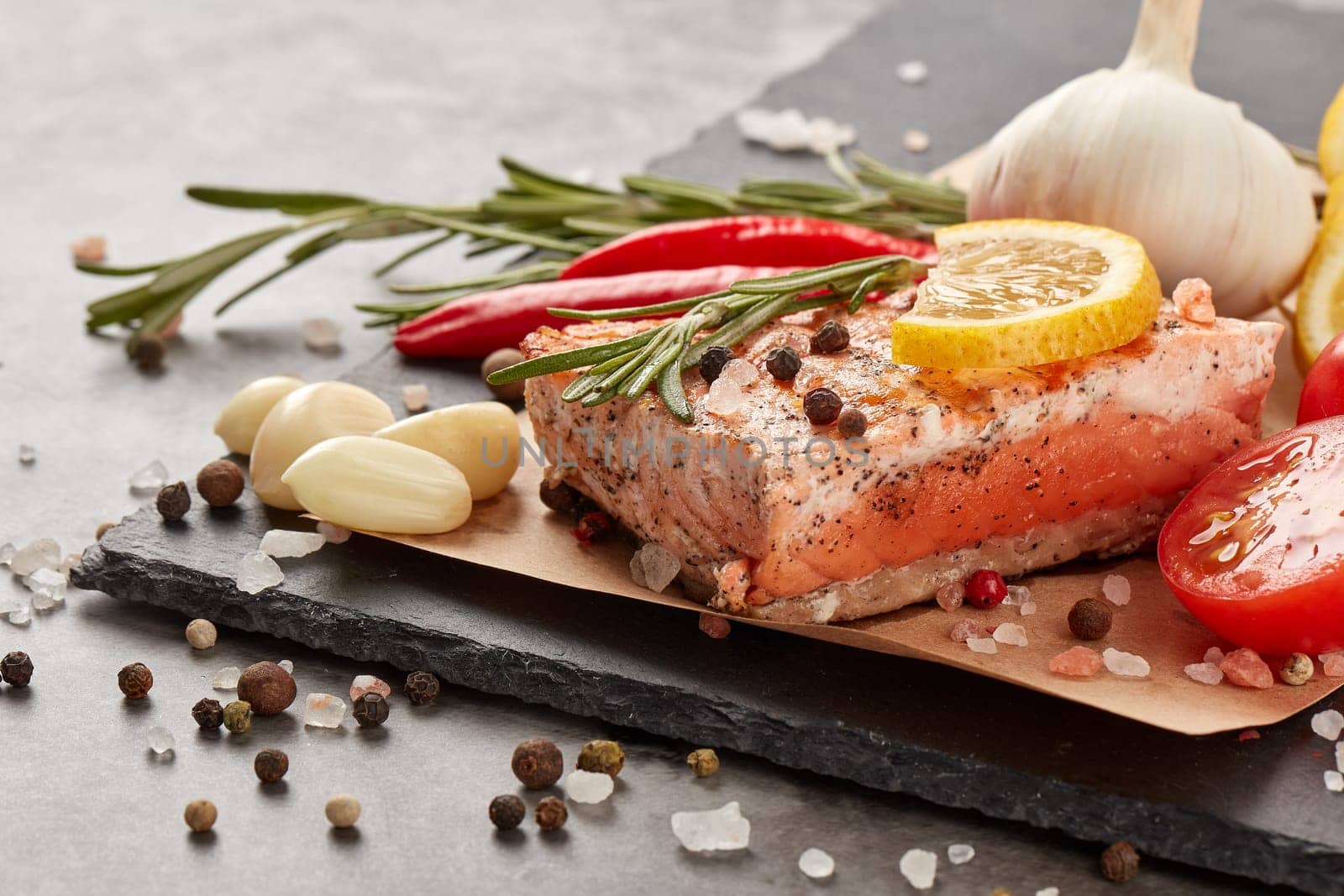 Grilled salmon fillet with spices and vegetables lying on stone cutting board on a grey background. Seafood menu.  Keto diet.
