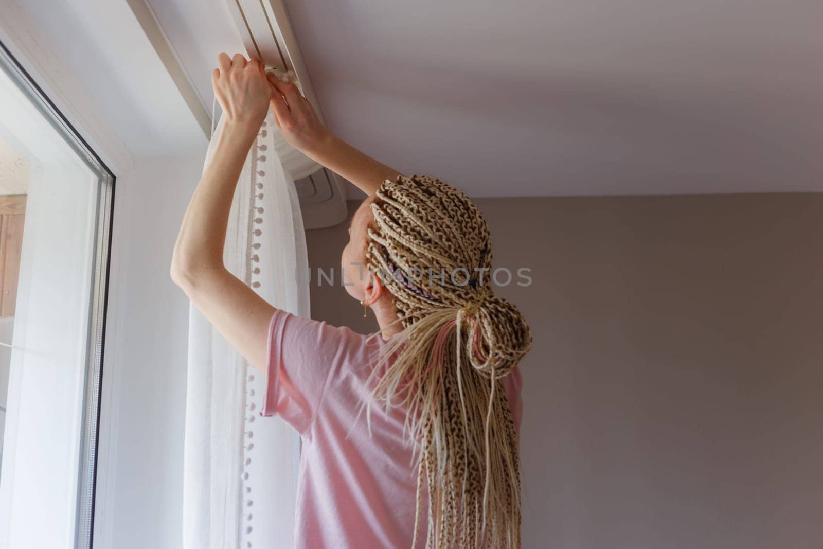 Young blonde woman hanging up curtains at the window