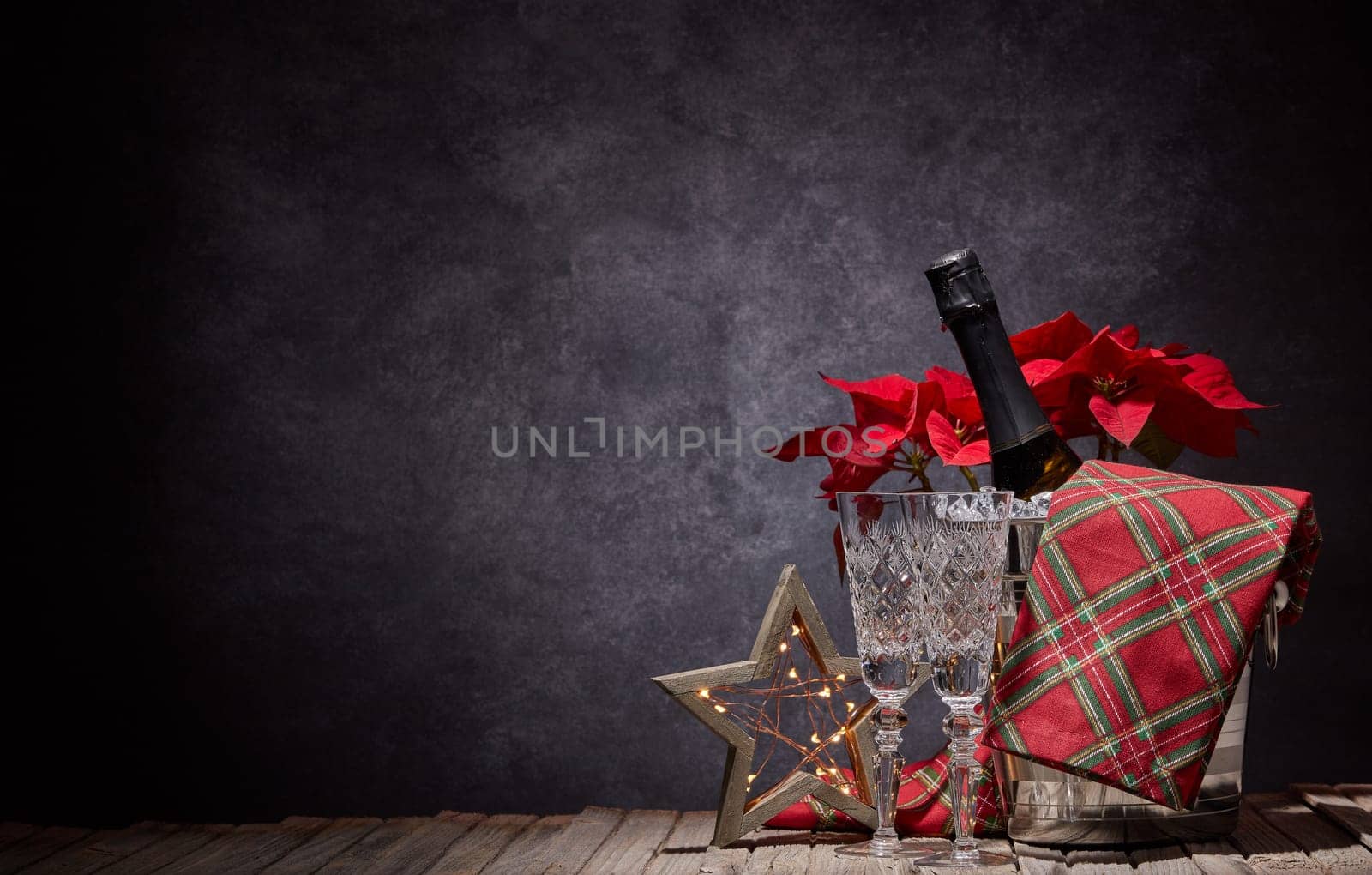 Champagne bottle in bucket with ice, empty champagne flutes and Christmas ornament on dark background with copy space. Christmas. New Year. Design element for greeting card, invitation, advertising