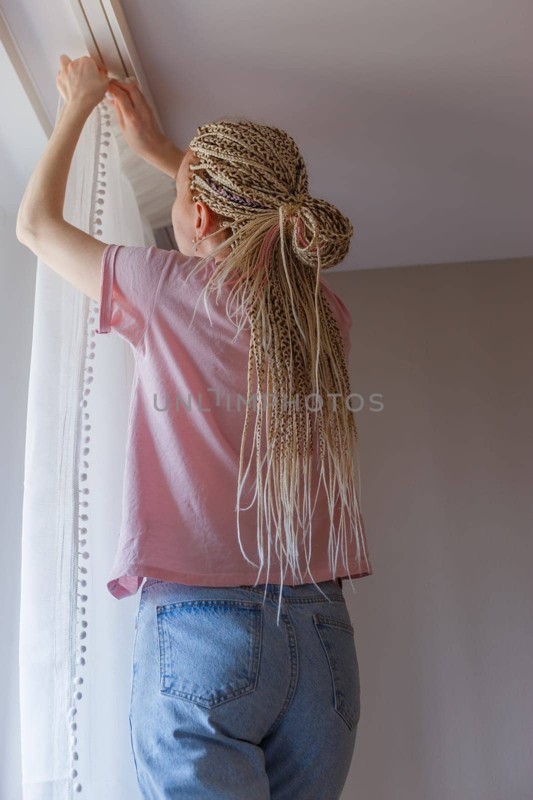 Young blonde woman hanging up curtains at the window