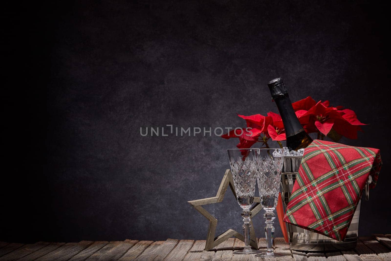 Champagne bottle in bucket with ice, empty champagne flutes and Christmas ornament on dark background with copy space. Christmas. New Year. Design element for greeting card, invitation, advertising