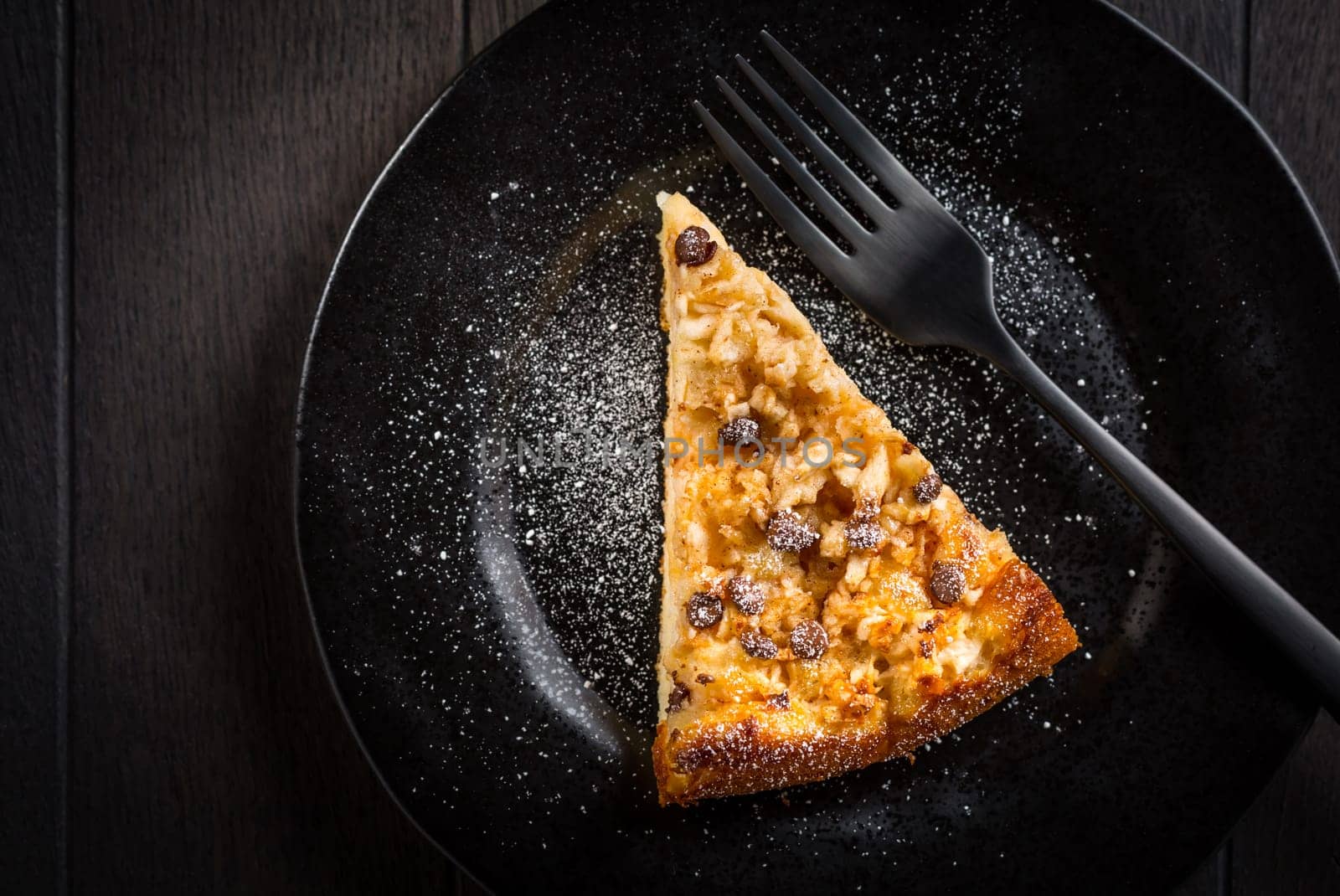 Piece of homemade apple pie with chocolate pieces for Thanksgiving on black plate