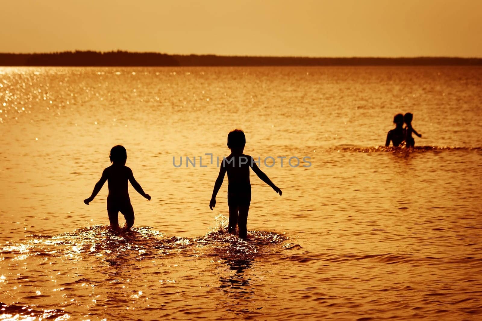 Children silhouettes in the water at sunset