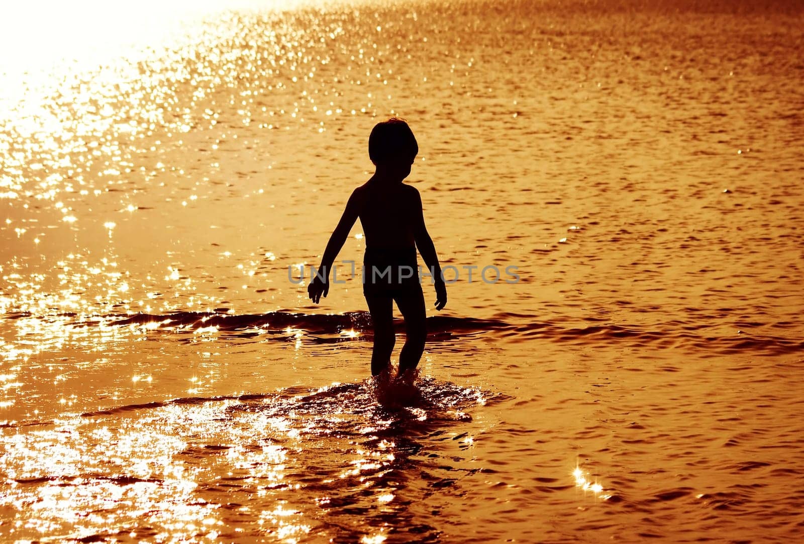 Children silhouettes in the water at sunset