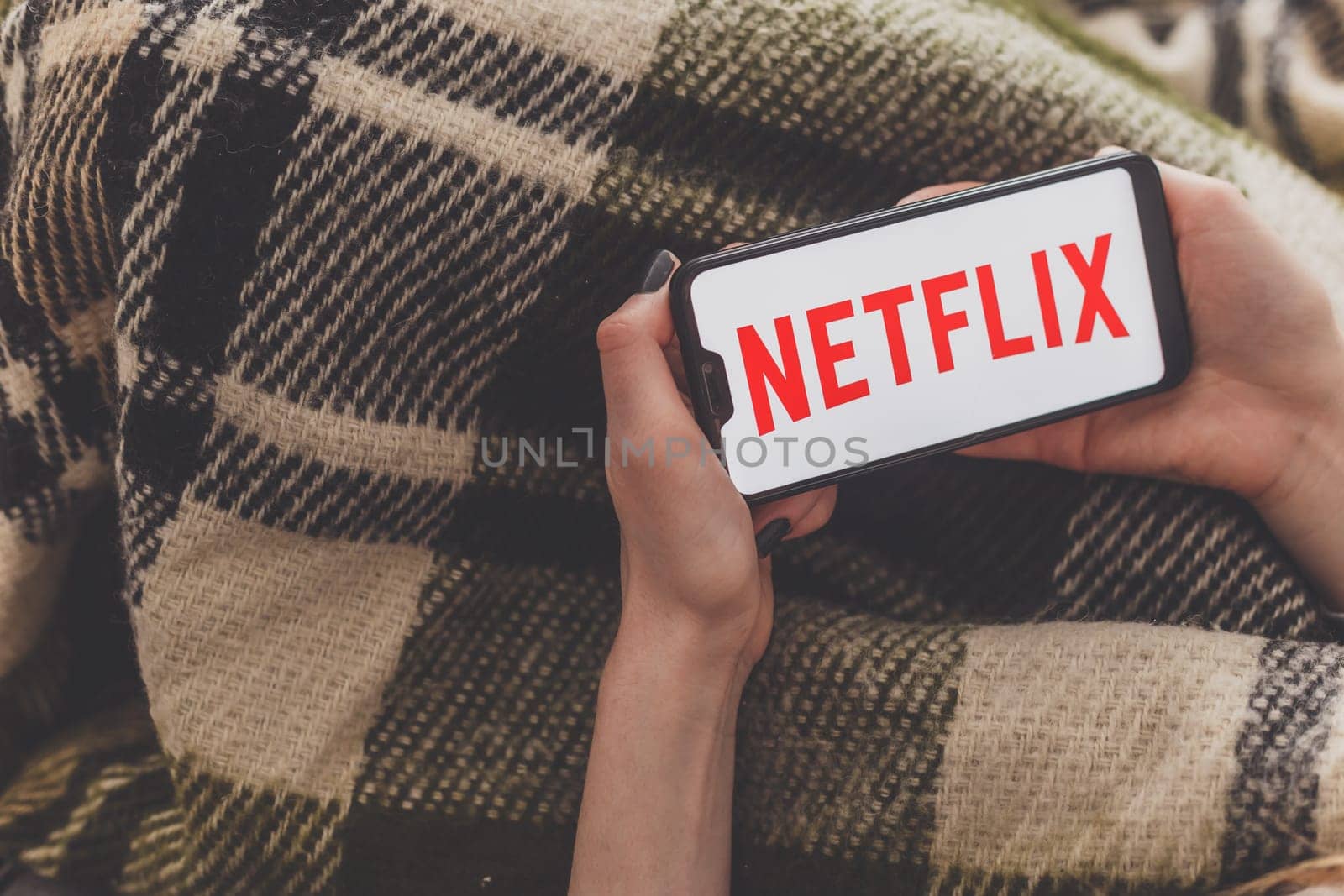 Minsk, Belarus - May 01, 2020: Woman during self isolation watching video by Netflix service on smartphone.