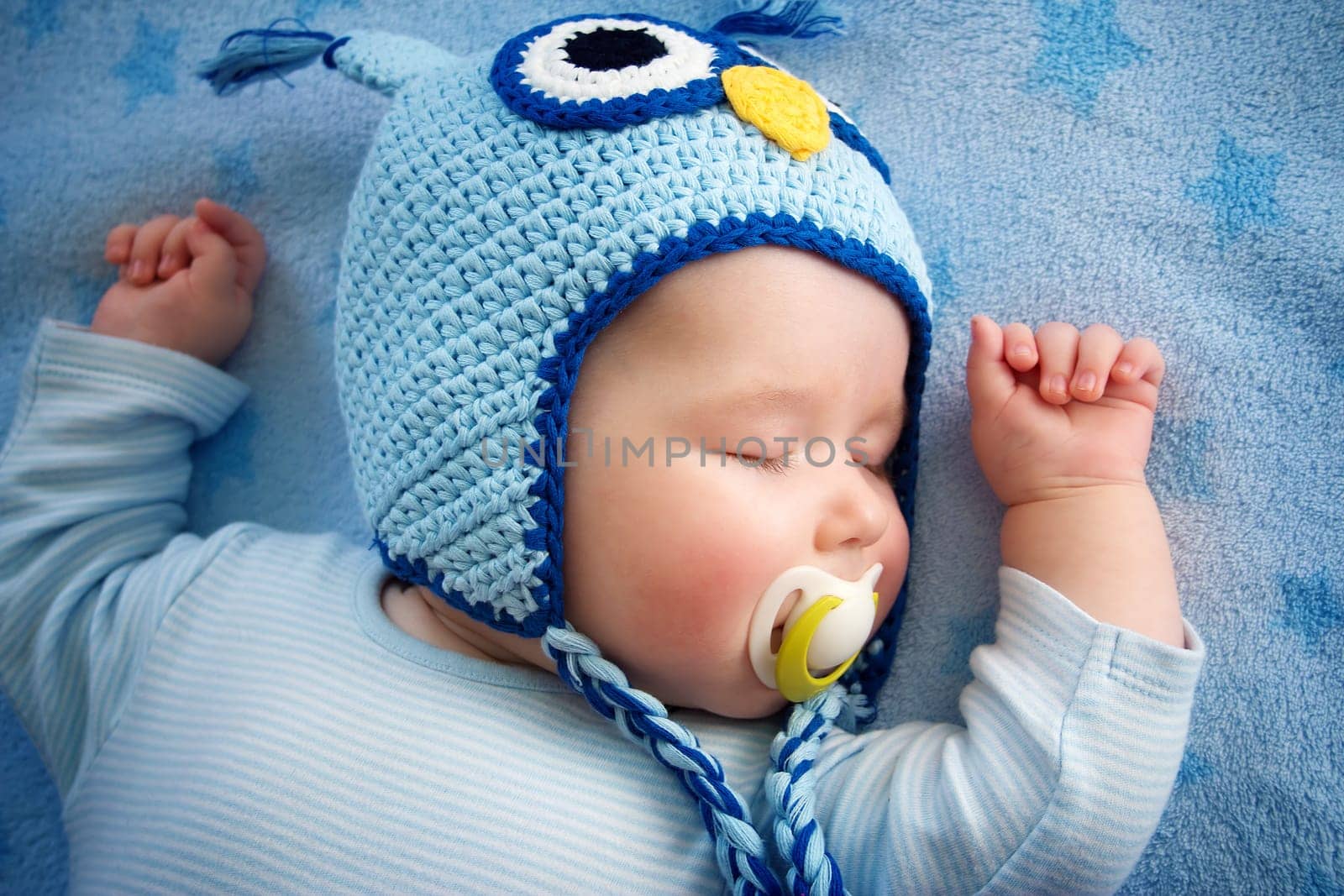4 month old baby in owl hat sleeping on blue blanket