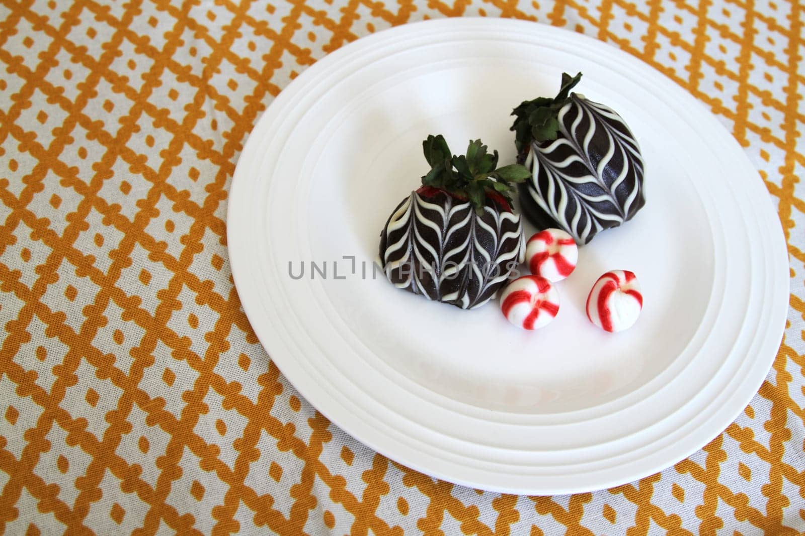 Chocolate covered strawberries with red and white peppermint hard candies on a plate on gold checkered tablecloth