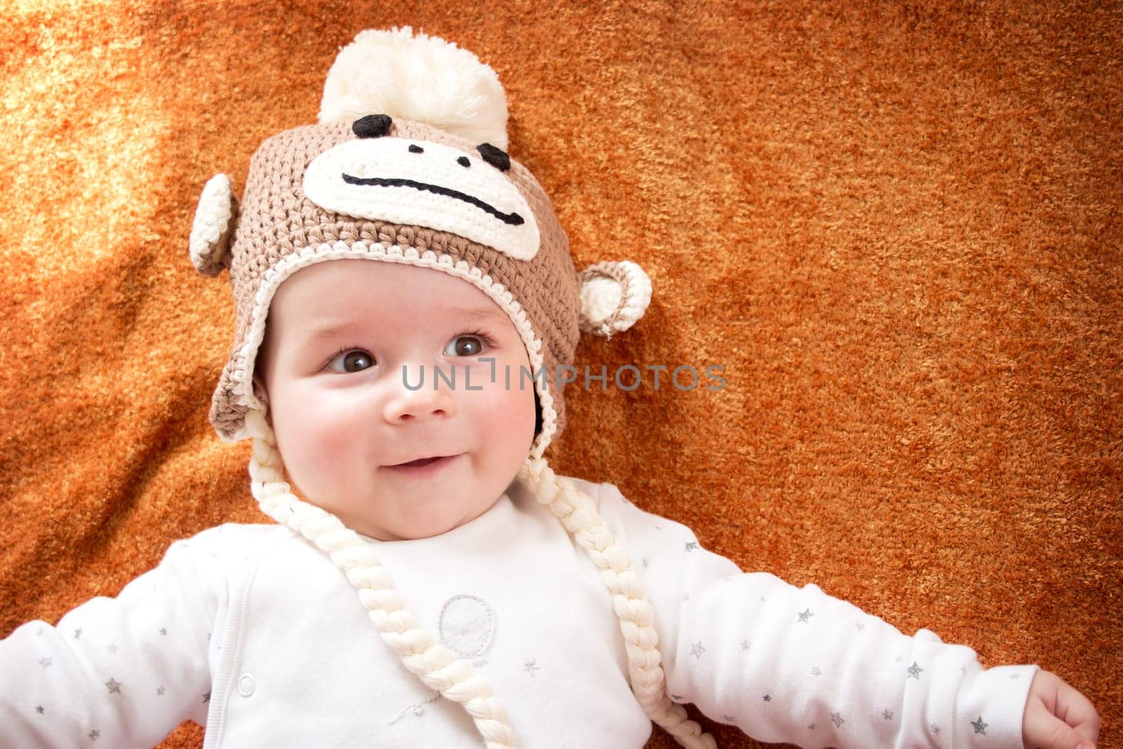 little baby in knitted montey hat on brown blanket