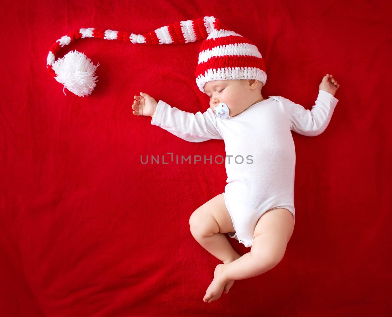 Little baby in knitted red whitey hat on red blanket