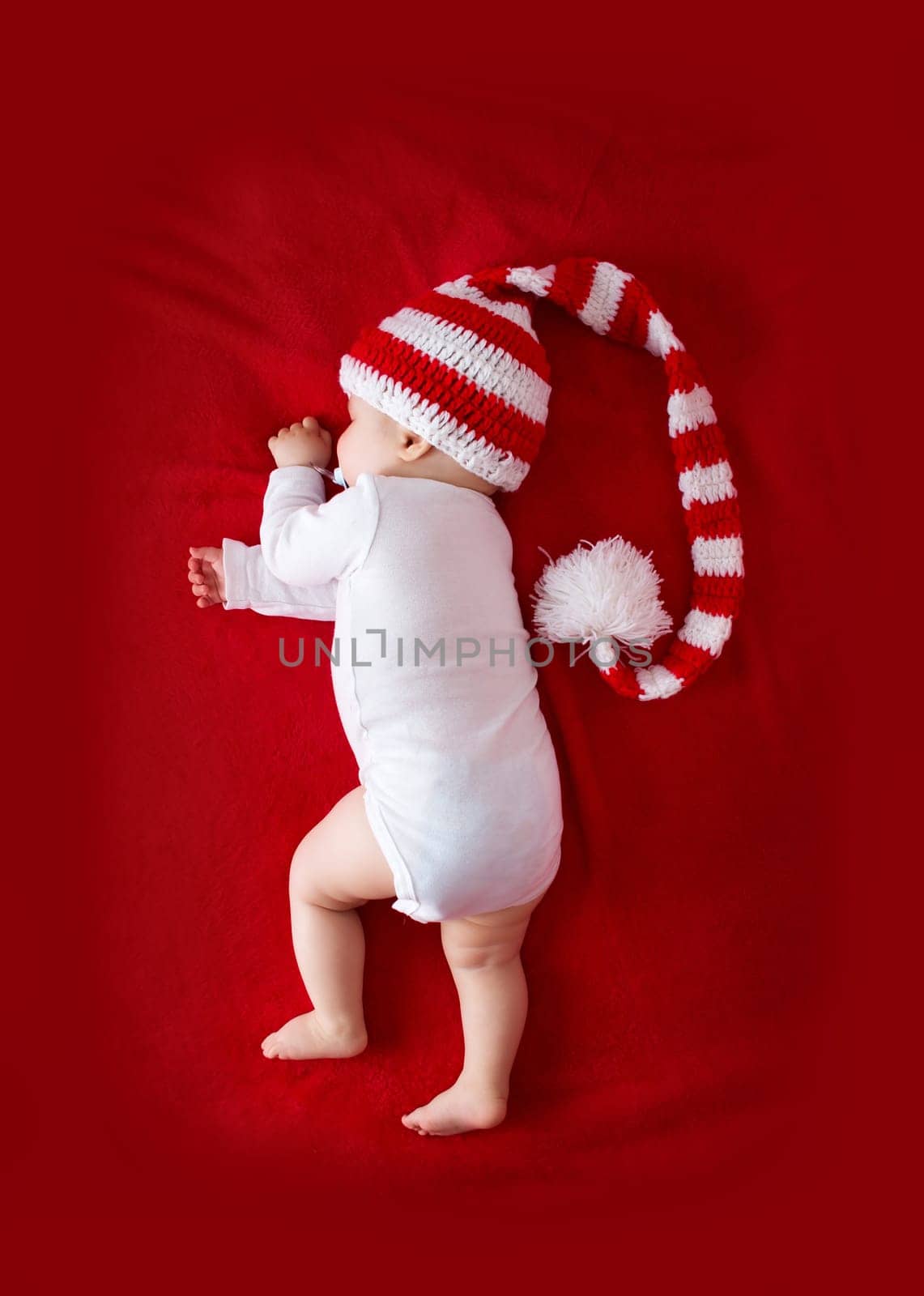 Little baby in knitted red whitey hat on red blanket
