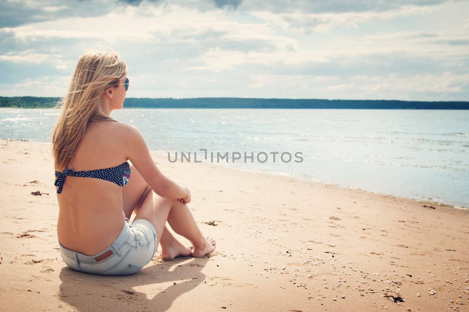 young woman sitting on the beach in sunglasses