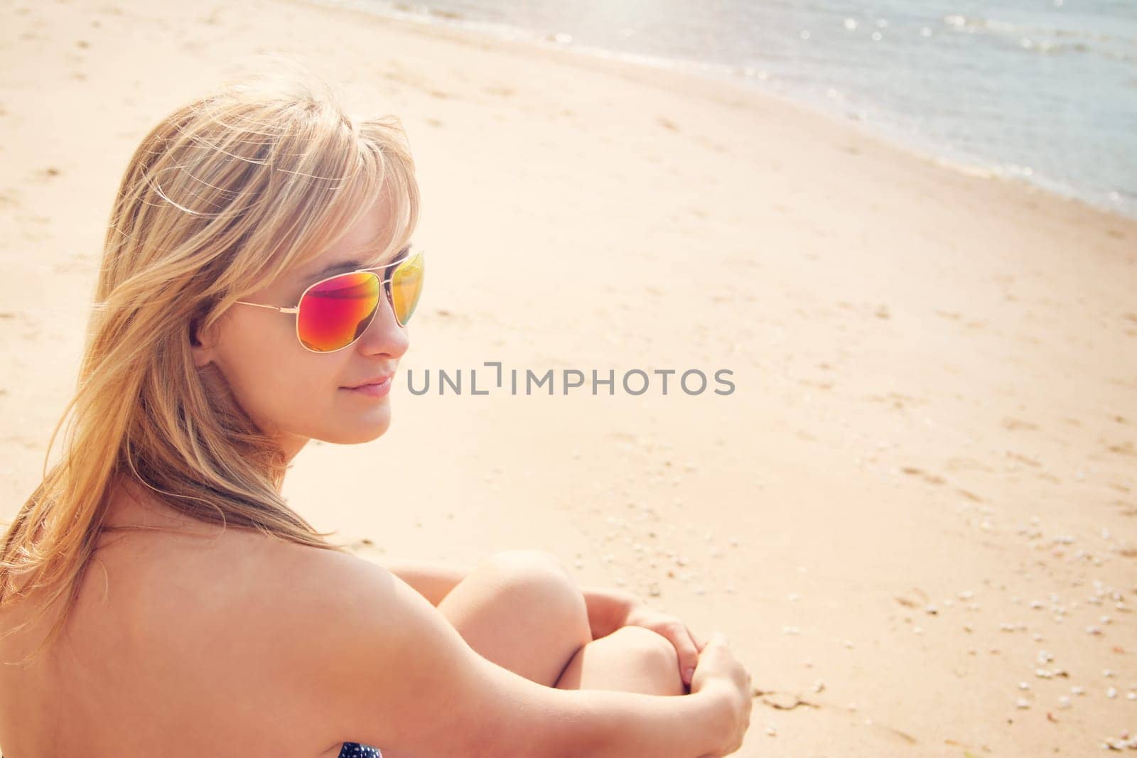 young woman sitting on the beach in sunglasses