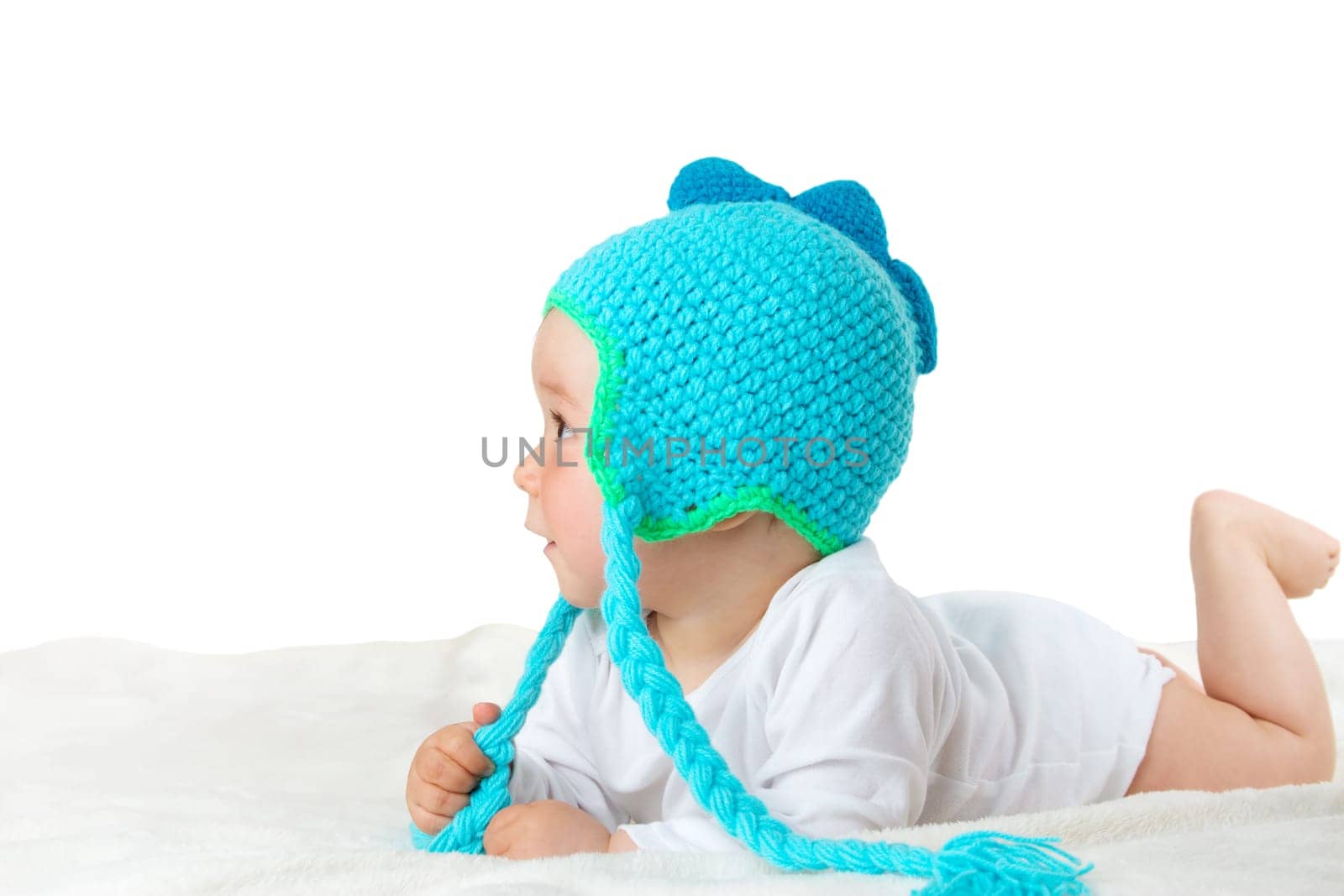 little baby in knitted dinosaur hat on soft blanket