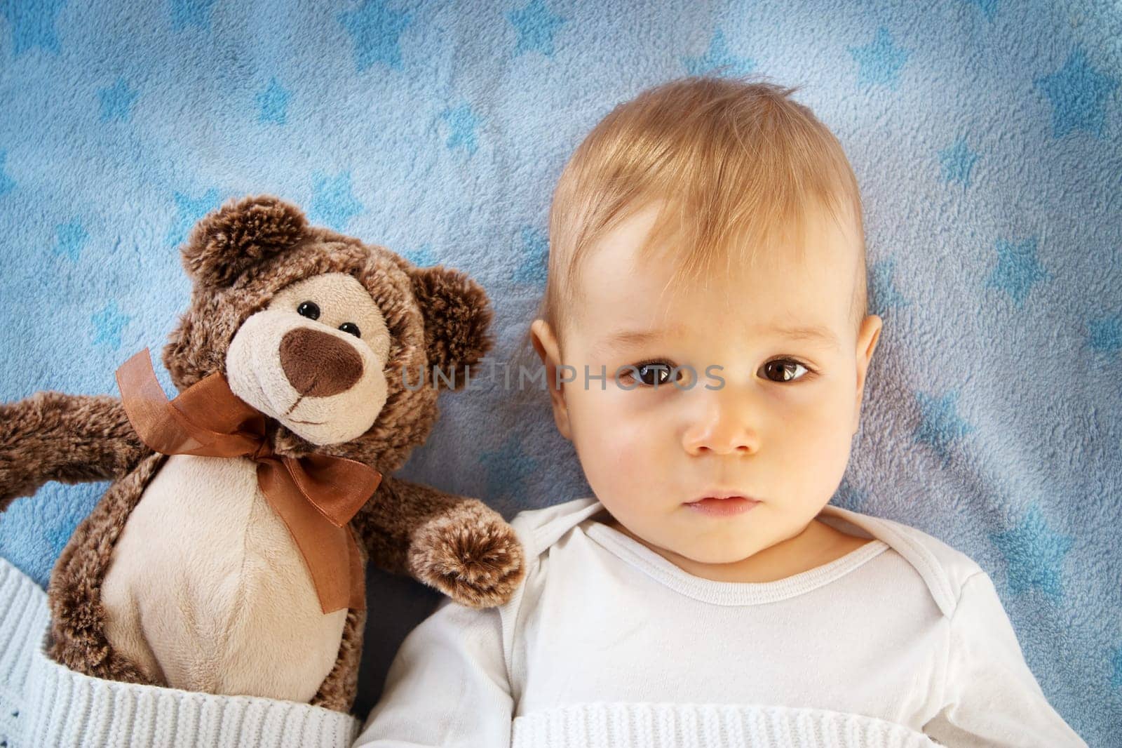 One year old baby lying in bed with a plush teddy bear
