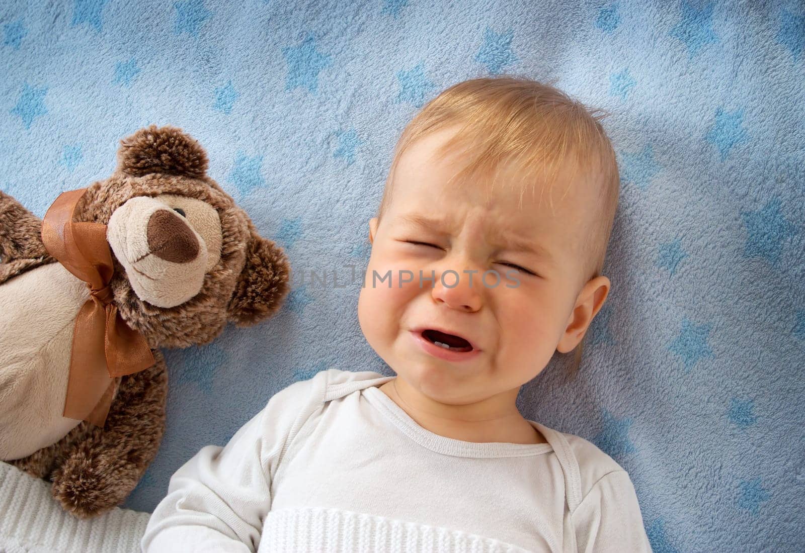 One year old baby crying in bed with a teddy bear