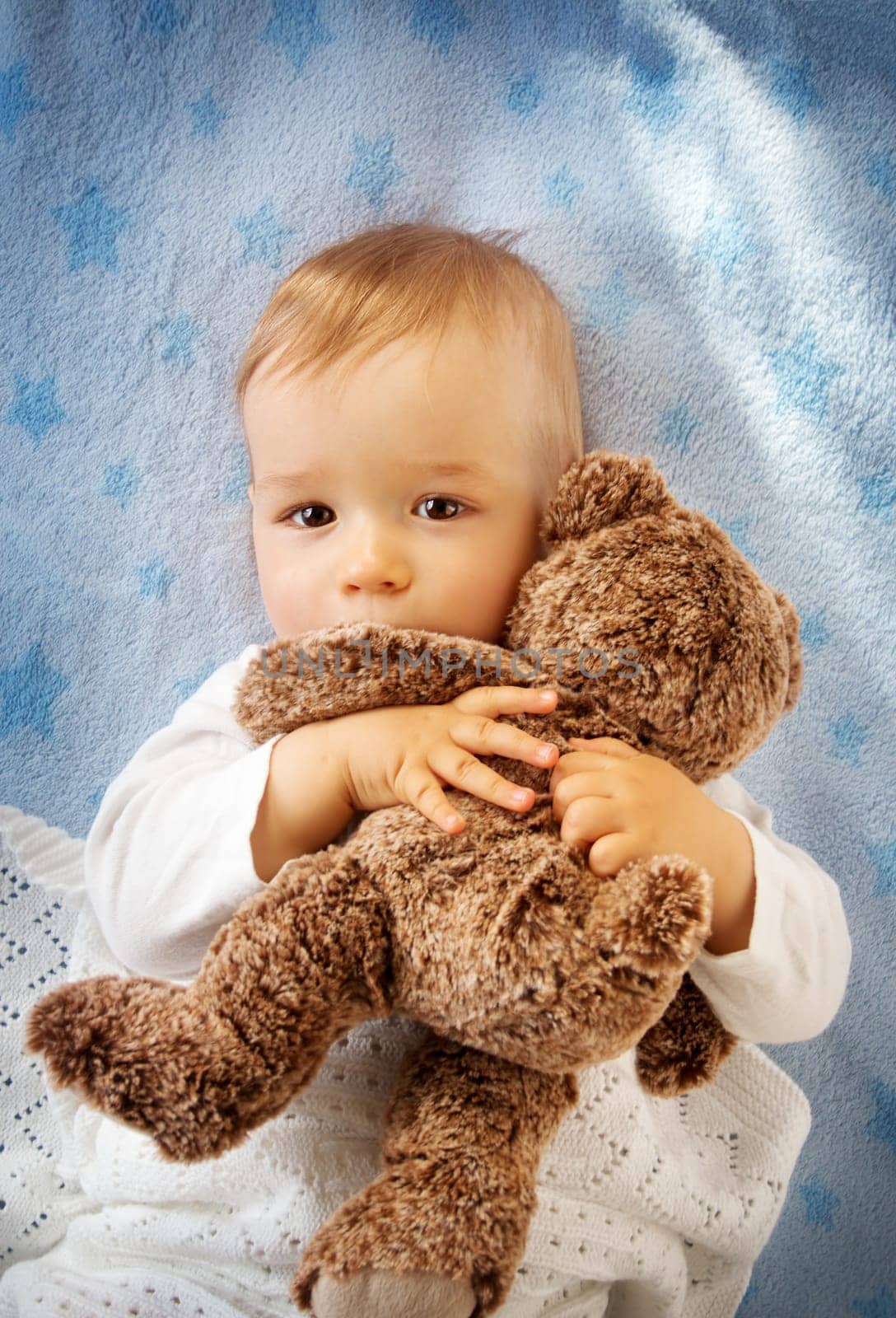 One year old baby lying in bed holding a plush teddy bear
