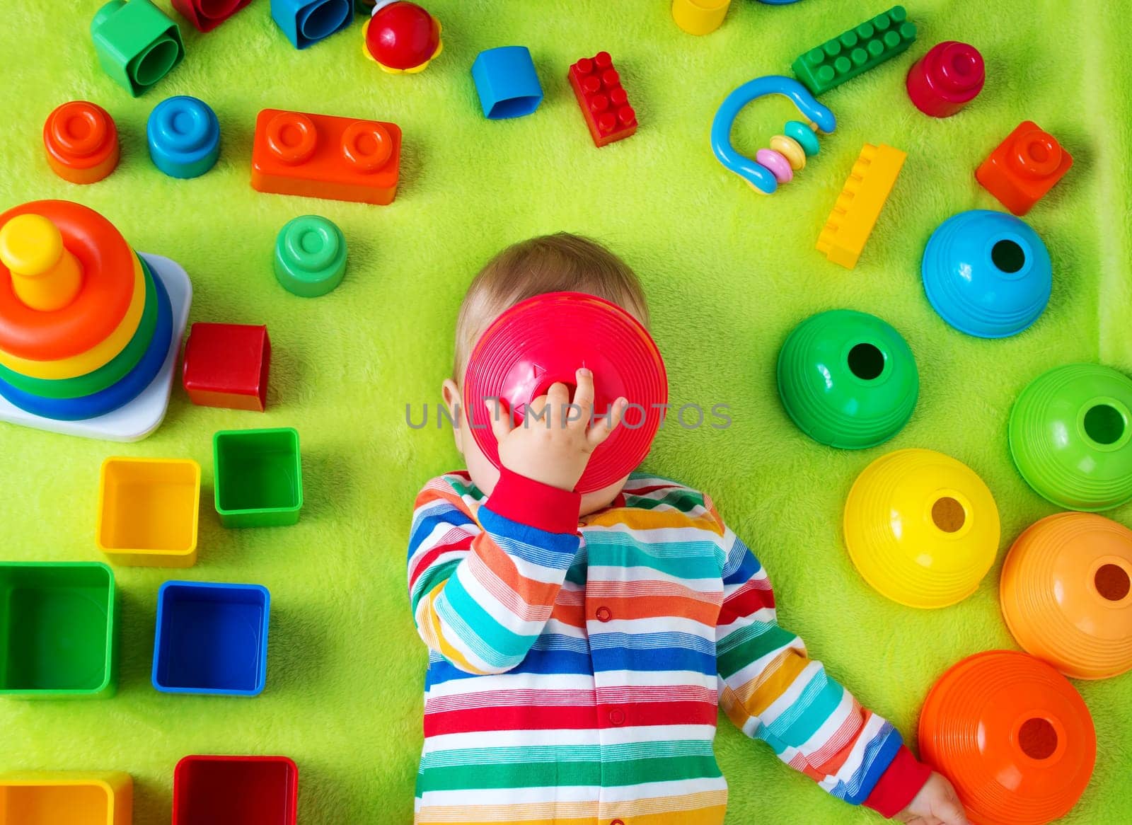 Baby boy lying on green blanket with many toys around