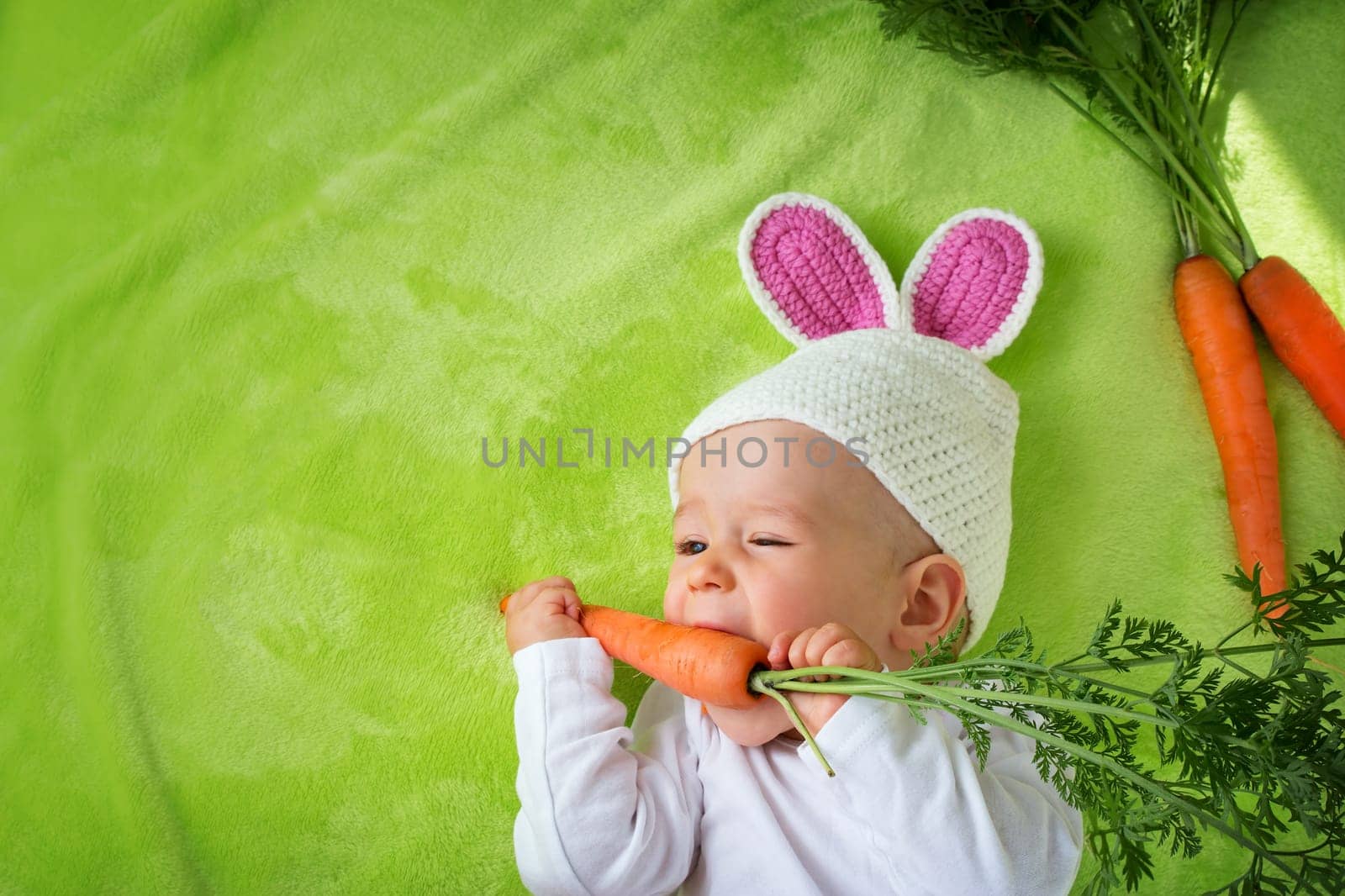 Baby in rabbit hat eating fresh carrot