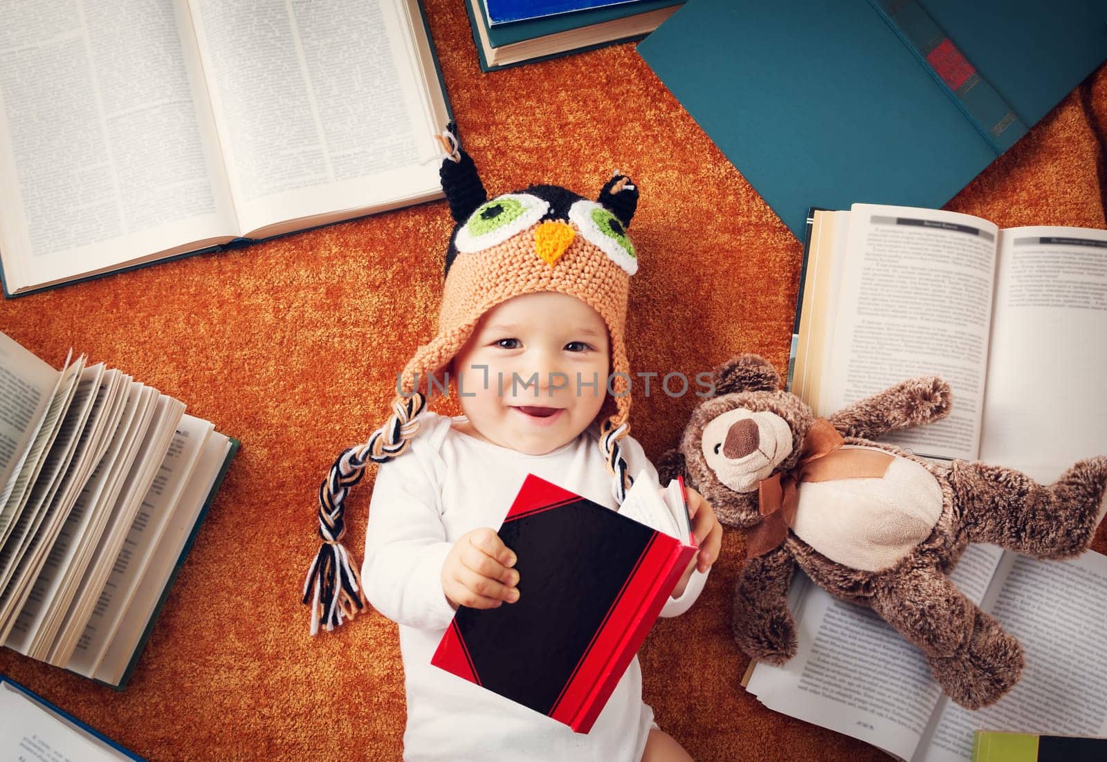 One year old baby in owl hat reading books with teddy bear