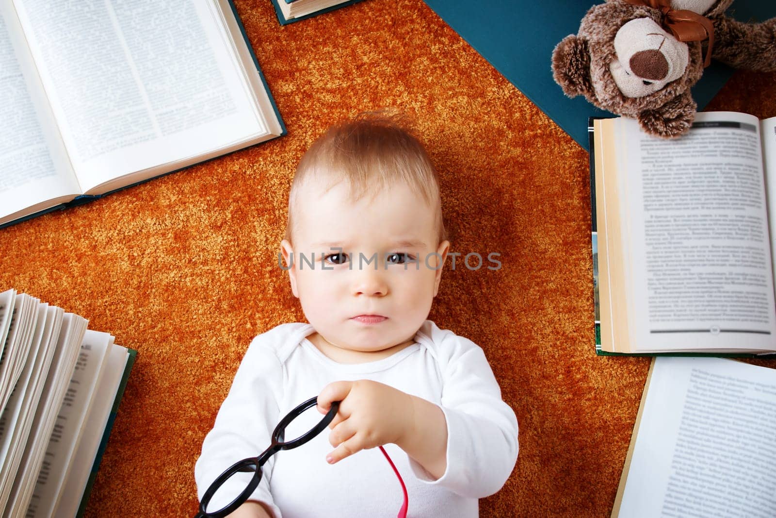 One year old baby among books with spectackles and a teddy bear