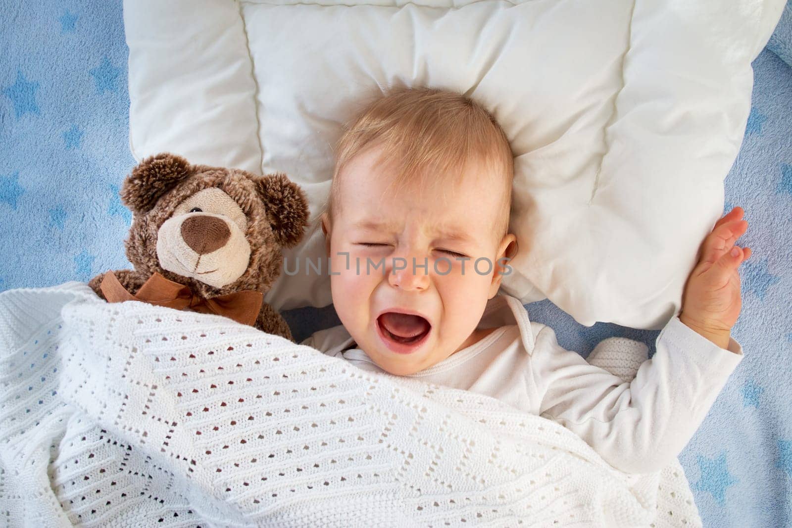 One year old baby crying in bed with a teddy bear