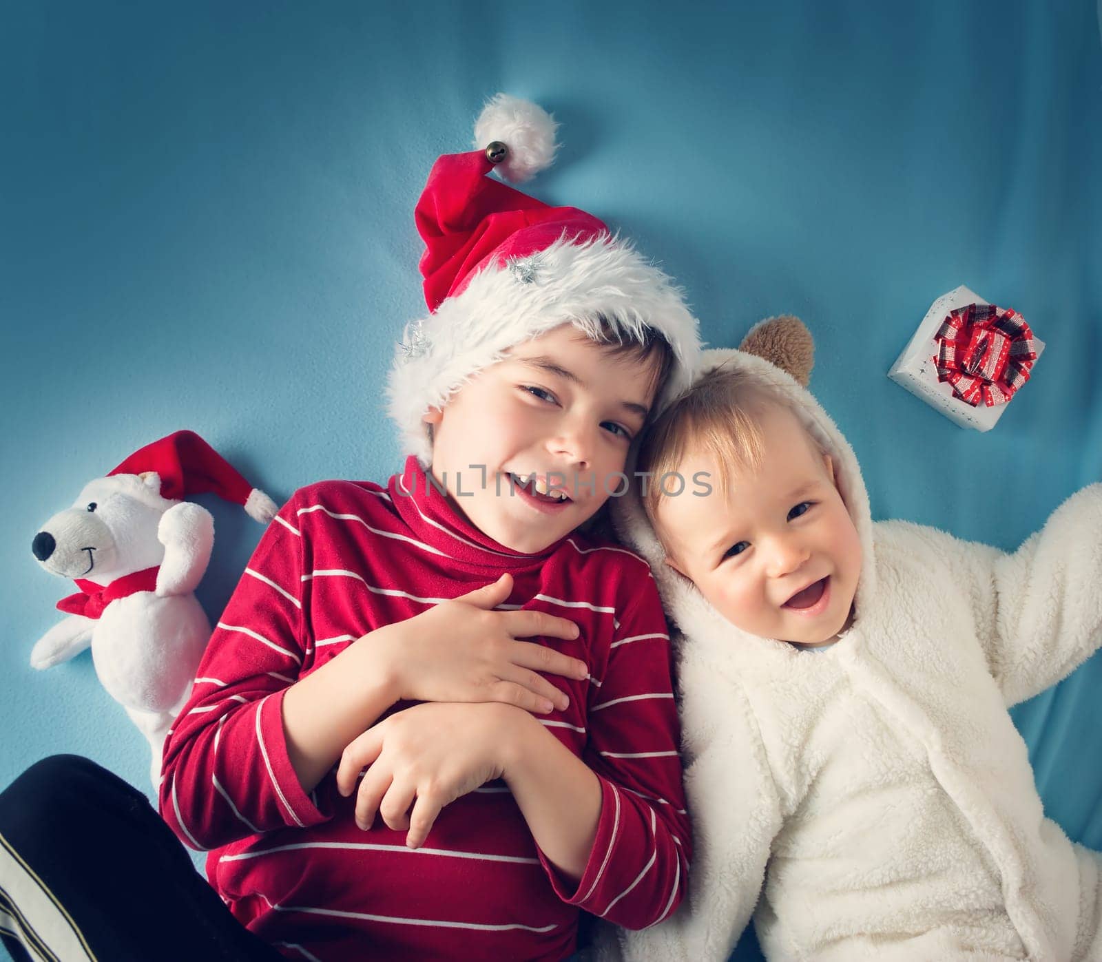 Two brothers, one and six years old in santa and bear costumes lying on blue blanket