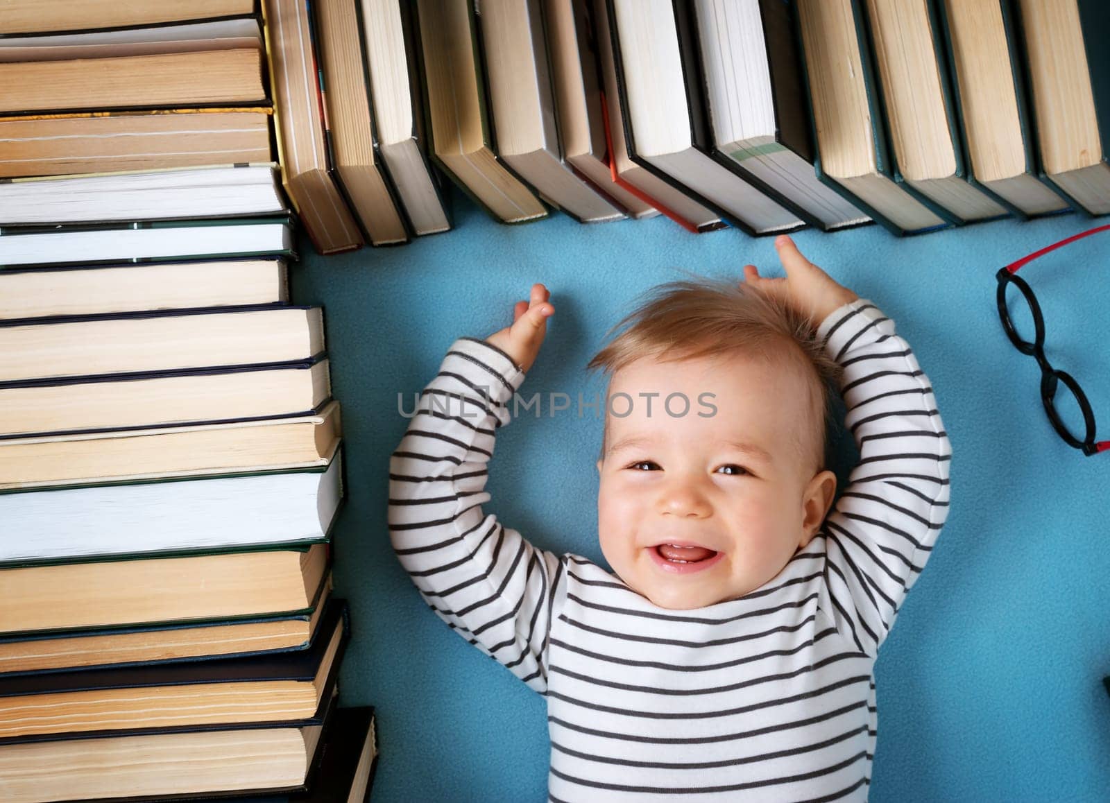 One year old baby among books with spectackle