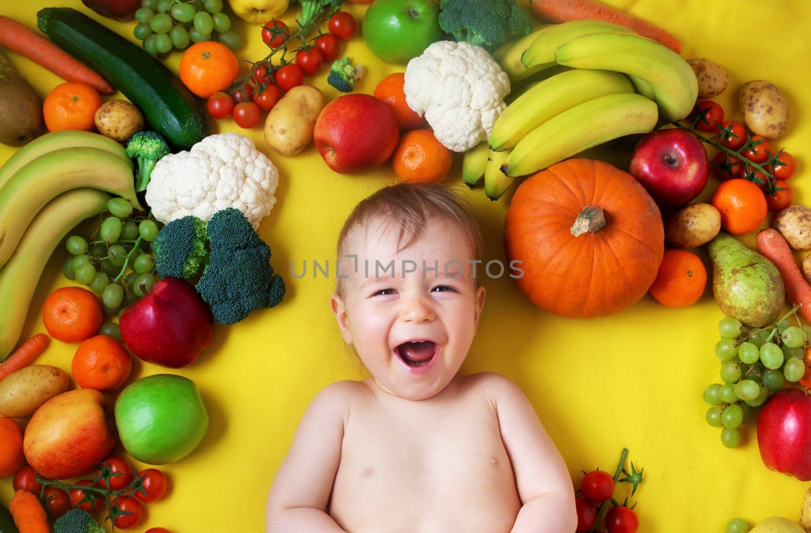 baby surrounded with fruits and vegetables on yellow blanket