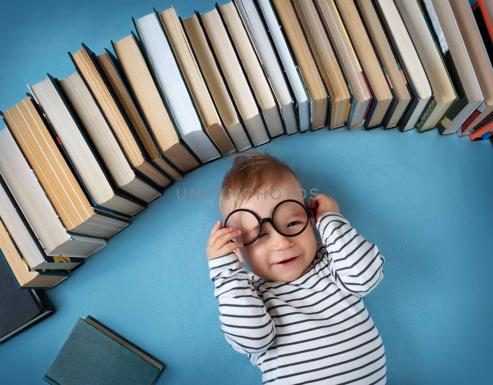 One year old baby among books with spectackle
