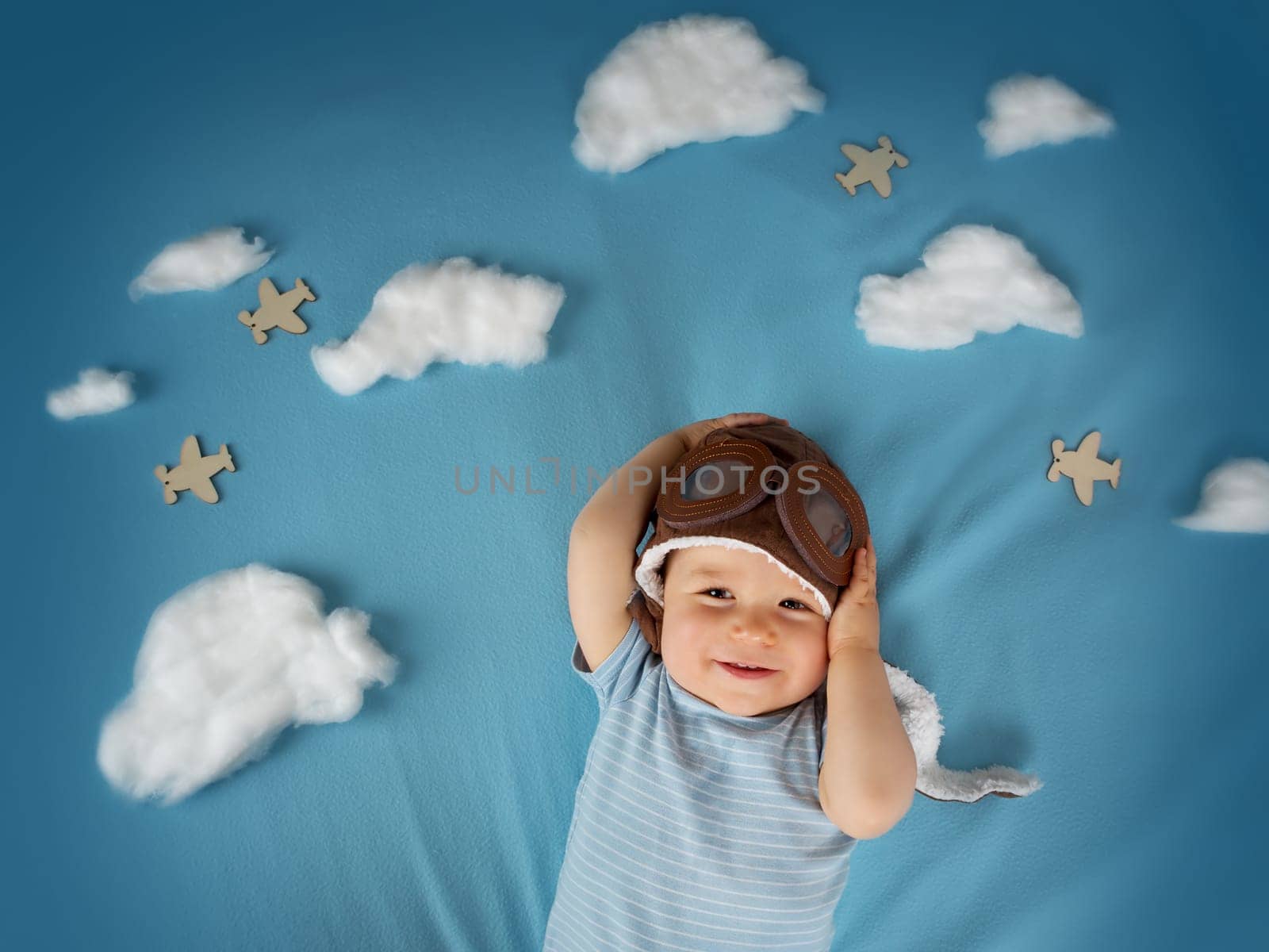 boy lying on blanket with white clouds in pilot hat