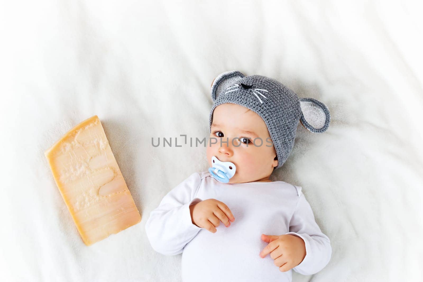 Baby boy in mouse hat lying on blanket with big piece of cheese