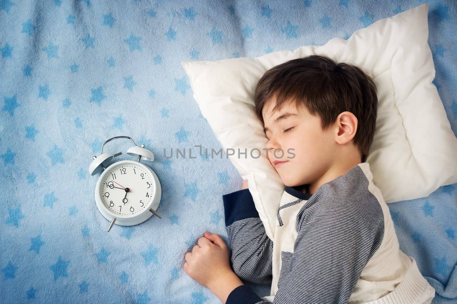 six years old child sleeping in bed on pillow with alarm clock
