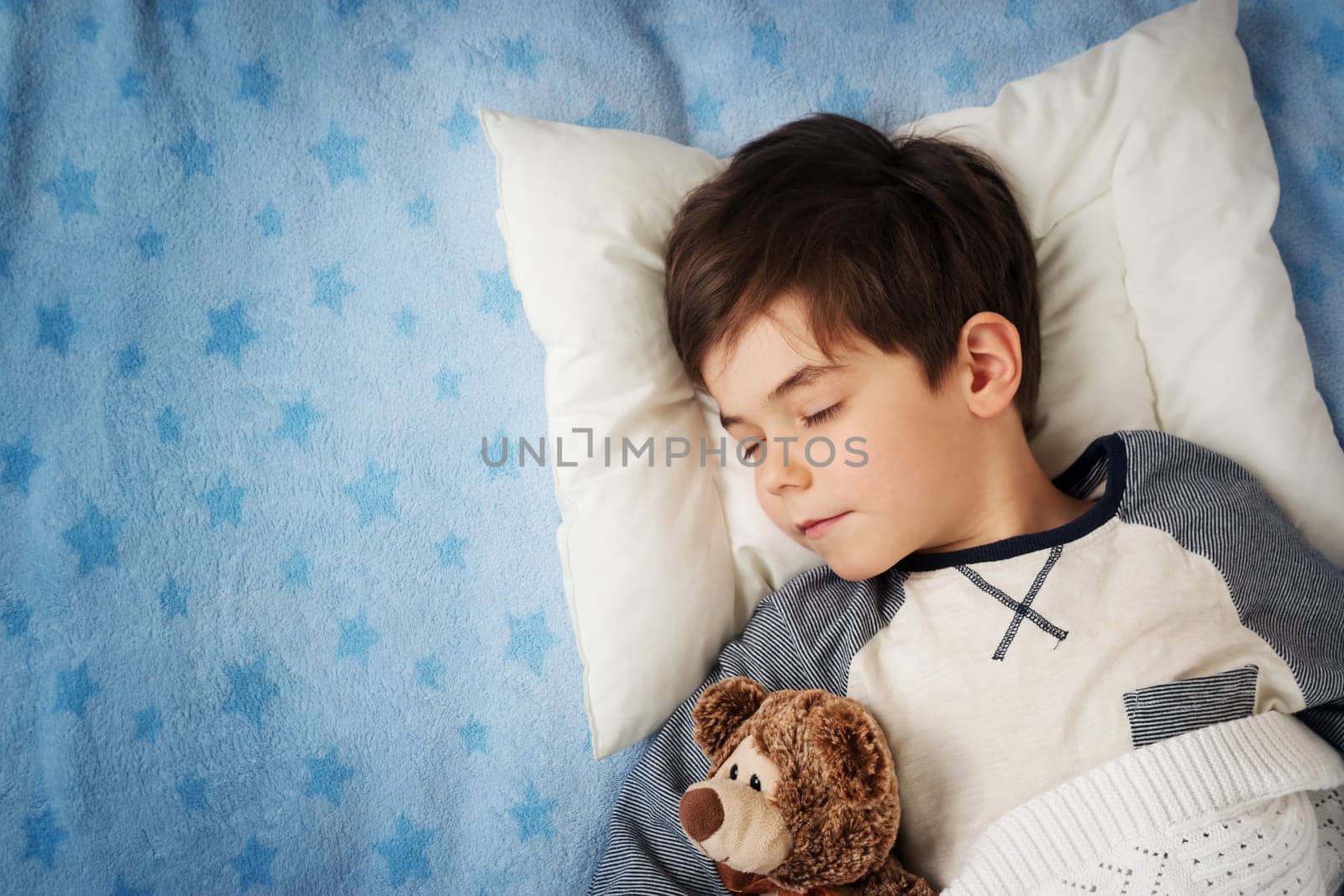 six years old child sleeping in bed on pillow with alarm clock and a teddy bear
