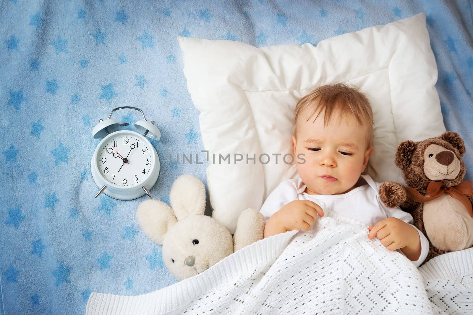 One year old baby lying in bed with alarm clock