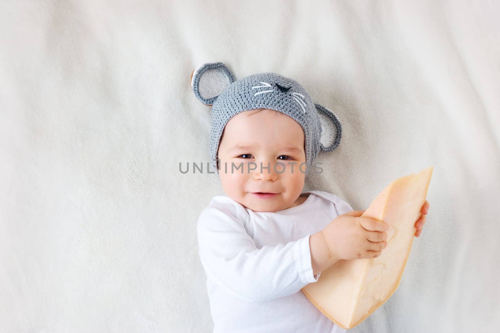 Baby boy in mouse hat lying on blanket with big piece of cheese