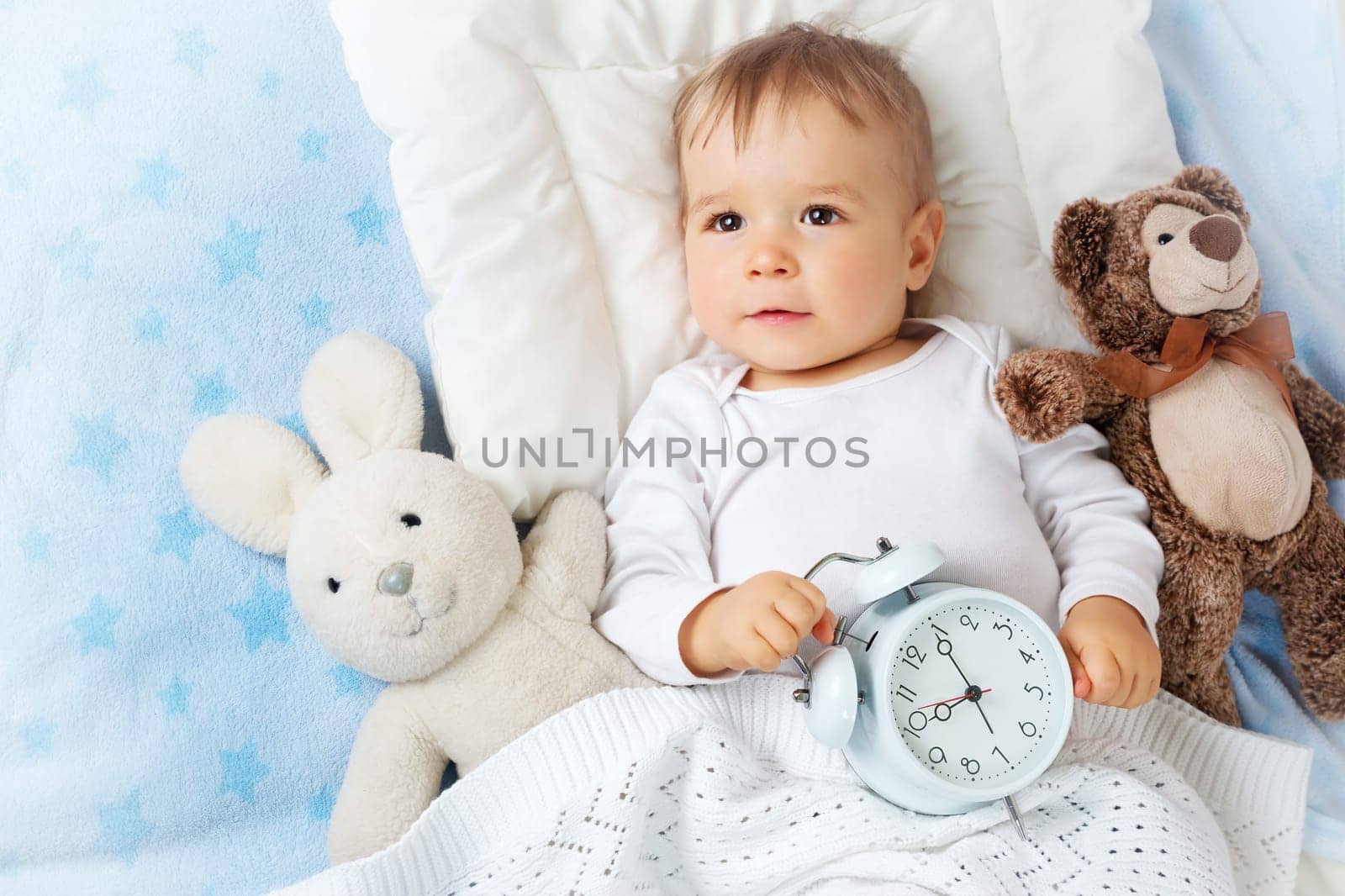 One year old baby lying in bed with alarm clock