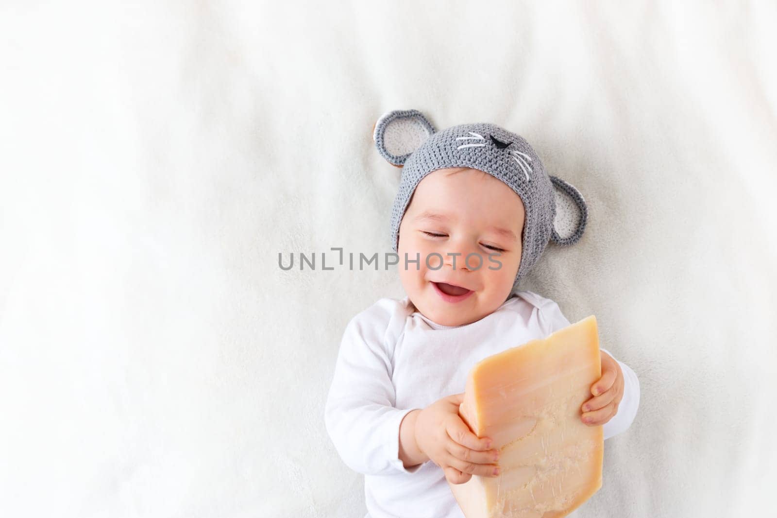 Baby boy in mouse hat lying on blanket with big piece of cheese