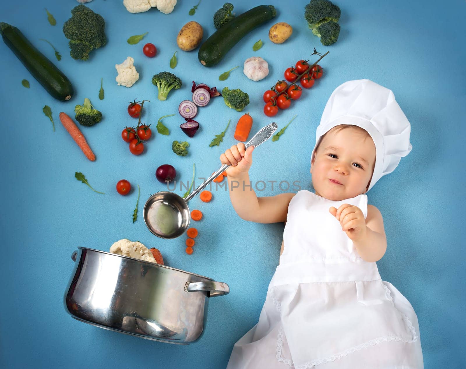 Baby boy in chef hat with cooking pan and raw vegetables
