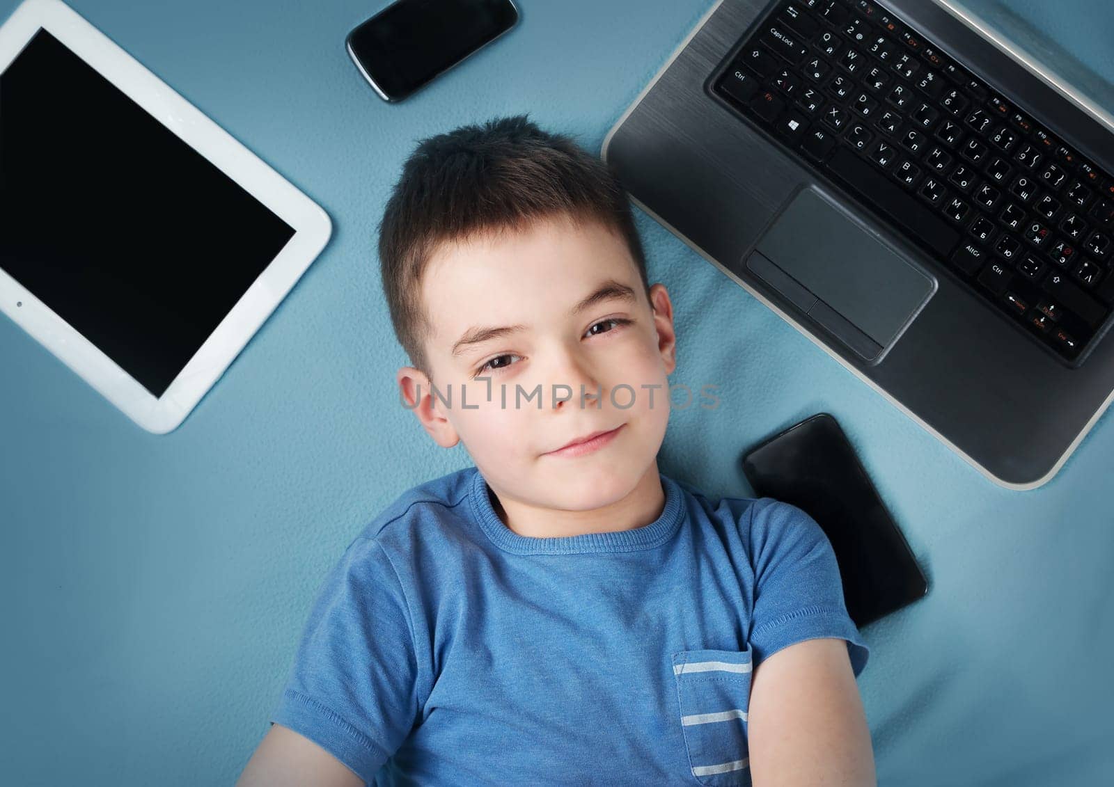 seven years old boy on blue blanket background with laptop, tablet, camera and phones