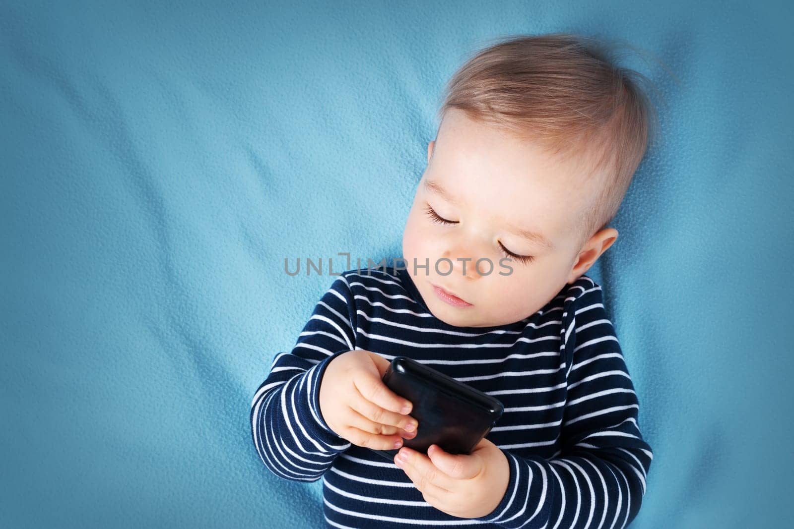 little boy on blue blanket background withcellphone