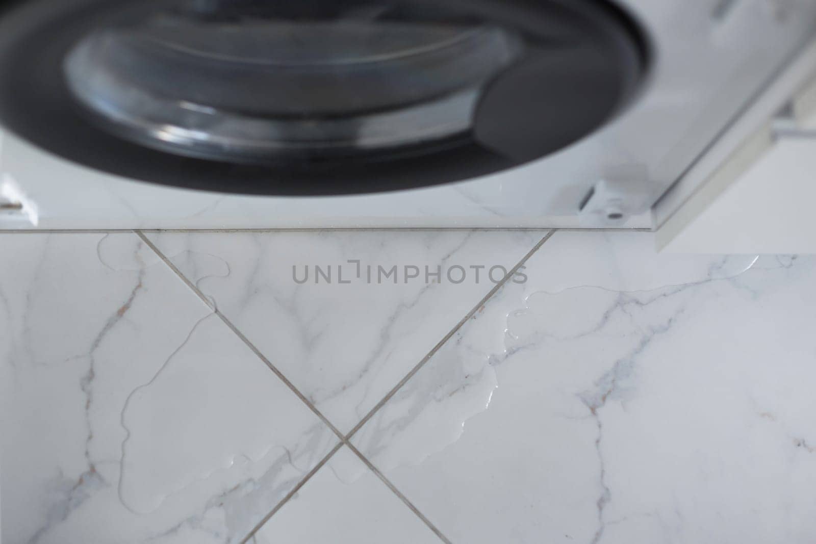 Spilled water leaked from washing machine built into the kitchen furniture. Spilled water on the tiled floor, flooding
