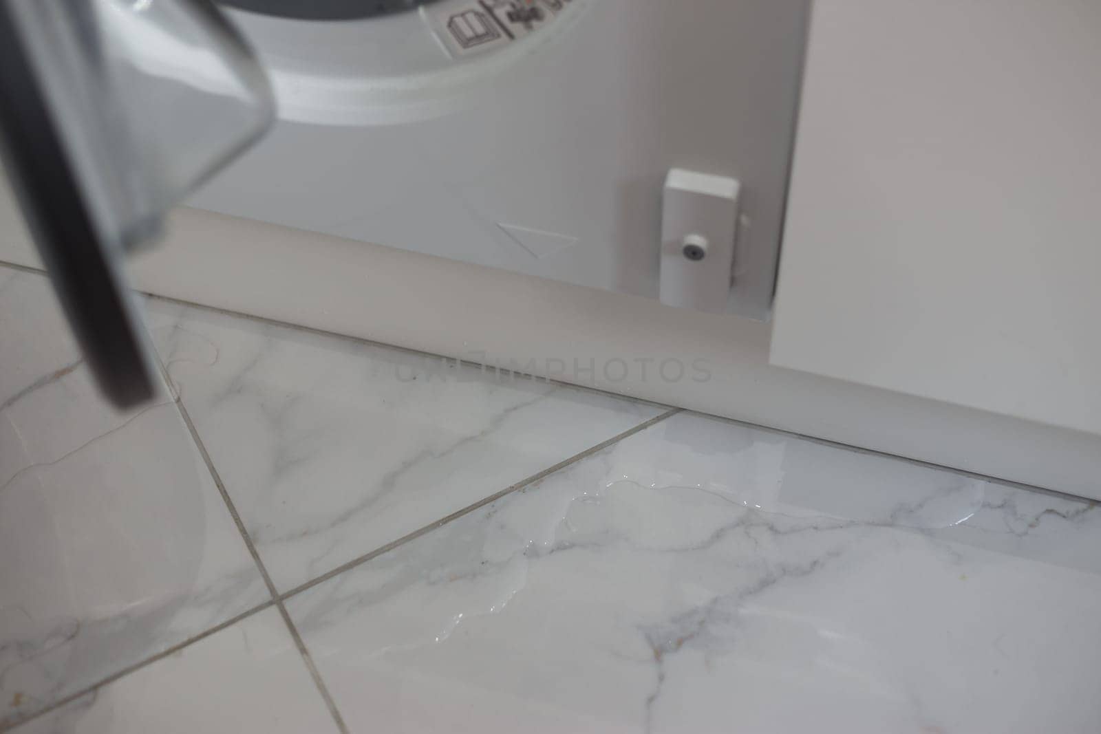 Spilled water leaked from washing machine built into the kitchen furniture. Spilled water on the tiled floor, flooding