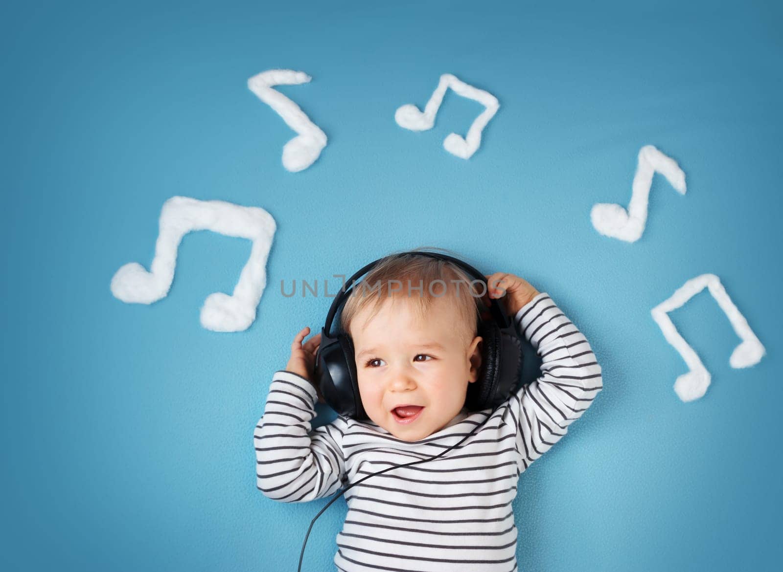 happy little boy on blue blanket background with headphones and musical notes on blue background